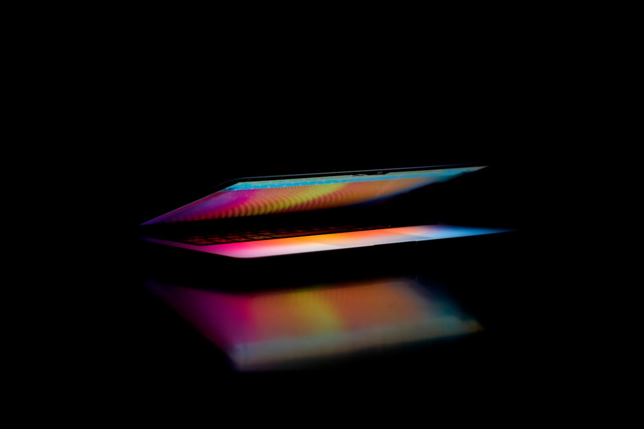 A colorful, partially open laptop screen reflects light in a dark setting.